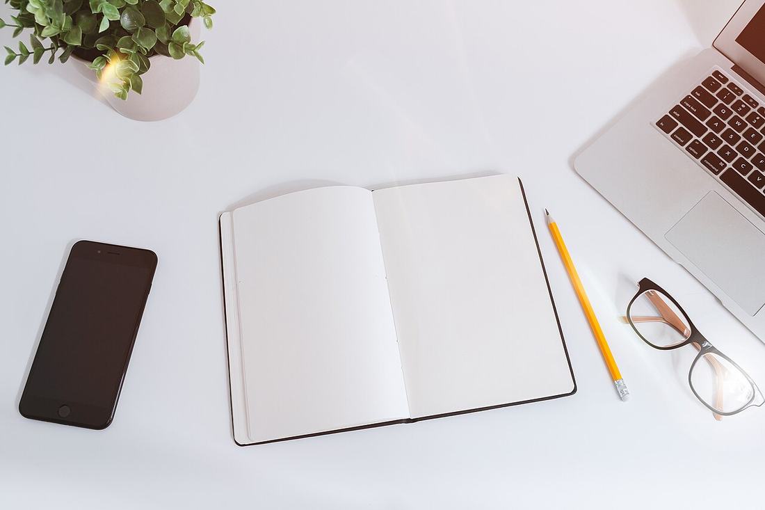 A blank notebook, phone, and laptop on a white work table
