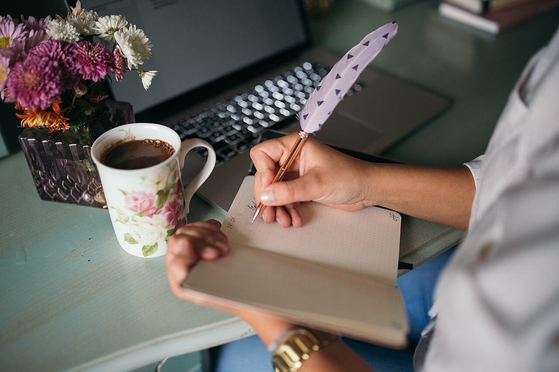 A hand writing notes in a notebook at a desk