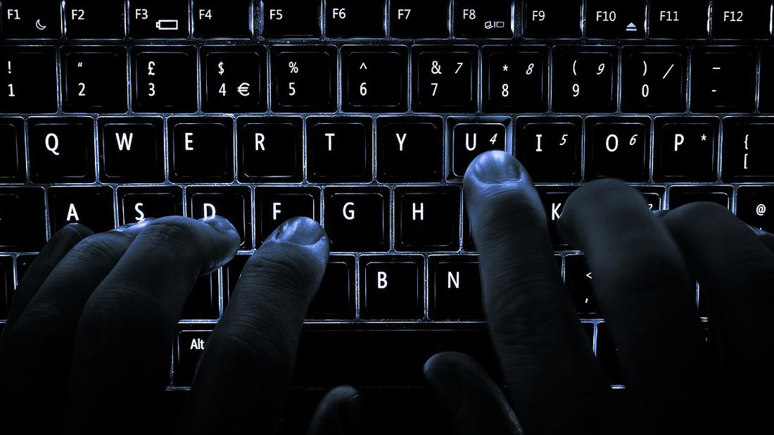 Hands typing on a backlit computer keyboard